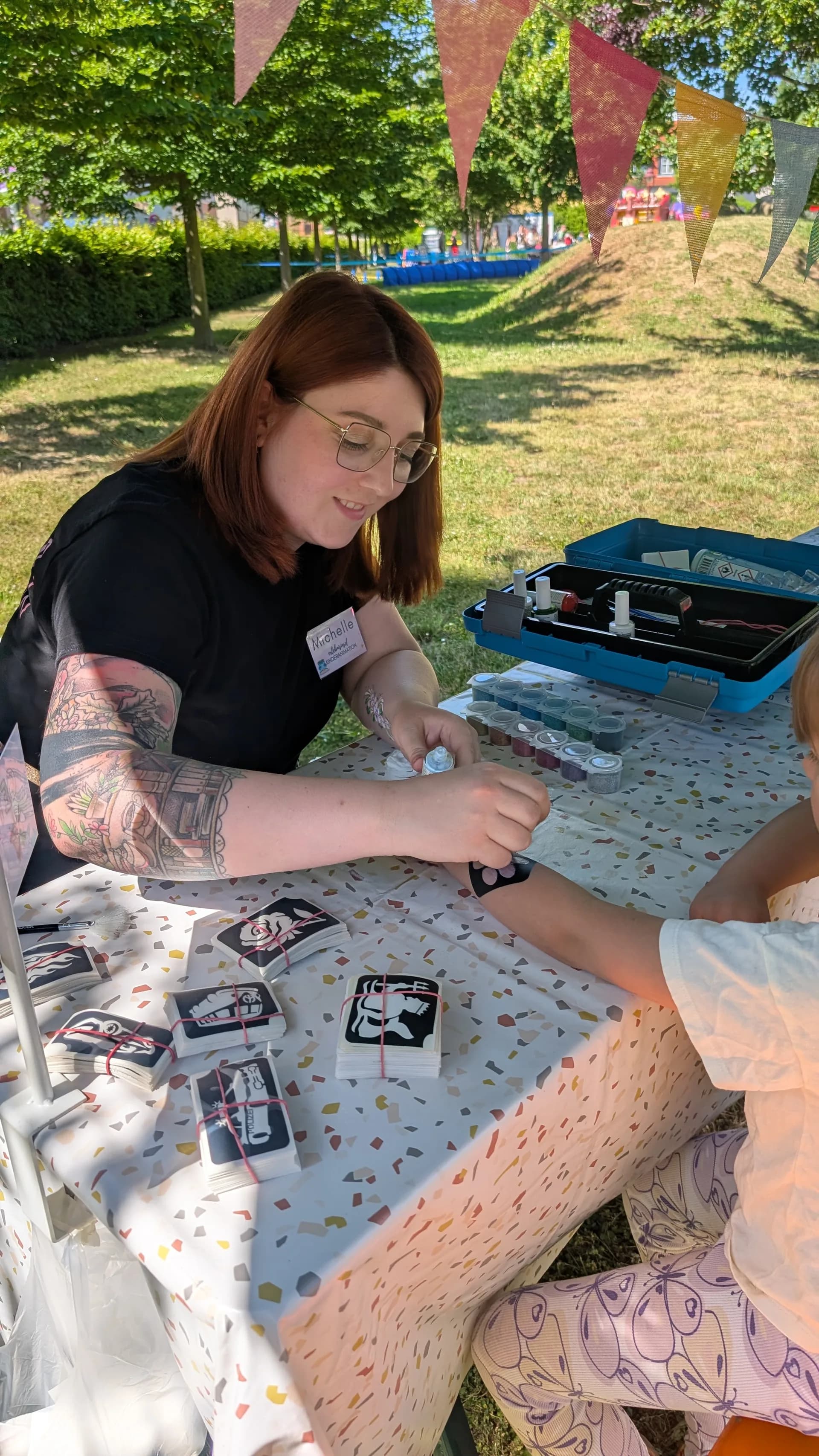 Mitarbeitern Michelle von der Erlebnisinsel gestaltet einem kleinen Jungen gerade ein Glitzertattoo